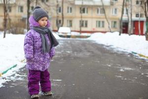 liten söt Lycklig flicka gående i de snö på en solig vinter- dag utomhus- foto