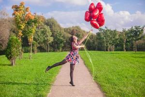 ung Lycklig flicka i färgrik klänning ha roligt med röd ballonger utanför foto