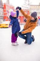 liten Lycklig flicka med ung far ha roligt på skridskoåkning rink foto