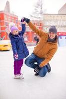 ung far och förtjusande liten flicka ha roligt på skridskoåkning rink foto