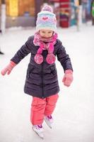 bedårande glad liten flicka som tycker om åka skridskor på isbanan foto