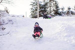 liten söt flicka drar en kälke i värma vinter- dag foto