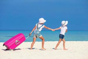 liten turister flickor med stor resväska på tropisk vit strand foto