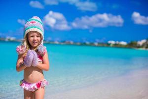 liten förtjusande flicka i värma stickat hatt och vantar på strand foto