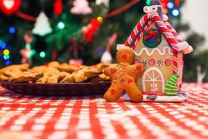 söt pepparkaka man i främre av hans godis ingefära hus bakgrund de jul träd lampor foto