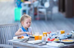 bedårande liten flicka äta frukost på uteservering foto