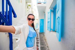 Lycklig kvinna tar selfie på folktom gator av grekisk by. ung skön kvinna på semester utforska europeisk stad foto