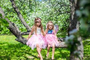 liten förtjusande flickor Sammanträde på blomstrande träd i äpple trädgård foto
