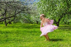 förtjusande liten flicka ha roligt i blomstrande äpple träd trädgård foto