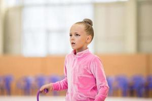 förtjusande liten flicka idrottare tåg i rytmisk gymnastik hall foto