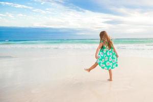 Fantastisk liten flicka på strand har en massa av roligt på sommar semester. förtjusande unge Hoppar på de havsstrand foto