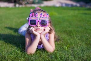 förtjusande liten flicka i Lycklig födelsedag glasögon leende utomhus- foto