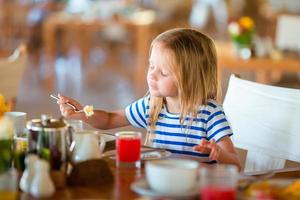 bedårande liten flicka äta frukost på uteservering foto