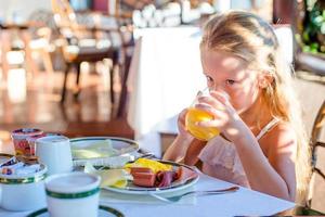 förtjusande liten flicka har frukost på restaurang foto