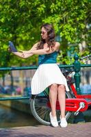 Lycklig ung kvinna med en stad Karta leende ridning på cykel foto