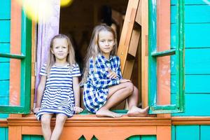 förtjusande liten flickor i de fönster av lantlig hus utomhus foto