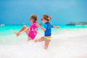 liten flickor har roligt på tropisk strand under sommar semester spelar tillsammans på grund vatten foto