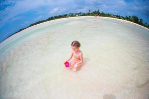 förtjusande liten flicka spelar med leksaker under strand semester foto