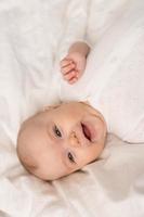 porträtt av en söt bebis i en vit kroppsdräkt på en säng på Hem med vit sängkläder. nyfödd bebis på Hem, Lycklig moderskap. hög kvalitet Foto