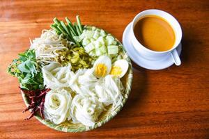 thai ris spaghetti - stänga upp thailand mat vermiceller nudel kokt ägg och färsk grönsaker på tallrik med curry soppa skål eras trä- tabell foto