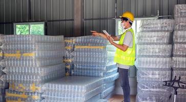 asiatisk man arbetstagare kontroll de stock av plast flaskor i de lager och jämförande de balansering siffra i de systemet efter leverans sändning. använder sig av en läsplatta till uppdatering uppkopplad stock foto