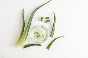 naturlig aloe vera gel i en glas skål på en vit bakgrund med bitar av färsk aloe och grön löv av de växt. platt layout. naturlig kosmetika. foto