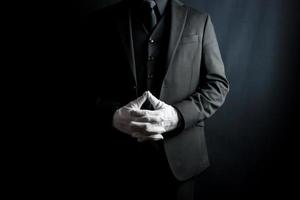 porträtt av herre i mörk kostym och vit handskar stående på svart bakgrund. professionell service och professionell gästfrihet. foto
