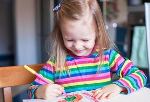 förtjusande liten flicka drar målarfärger Sammanträde på de tabell foto