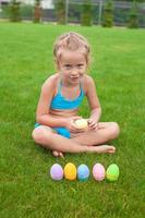 liten flicka med påsk ägg på de gräs i henne gård foto
