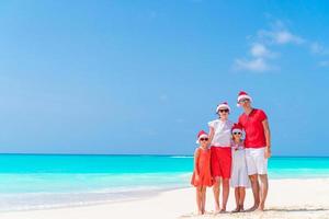 Lycklig familj i röd santa hattar på en tropisk strand fira jul semester foto