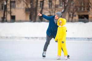 liten flicka inlärning till skridsko med henne far på isbana utomhus foto