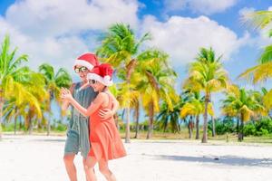 liten förtjusande flickor i santa hattar under strand semester ha roligt tillsammans foto