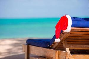 Sol vilstol med santa hatt på skön tropisk strand med vit sand och turkos vatten foto