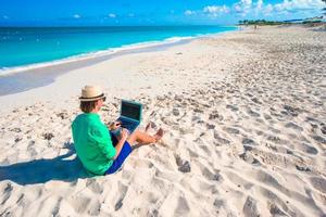 ung man med läsplatta dator och cell telefon på tropisk strand foto