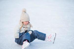 liten förtjusande flicka Sammanträde på is med skridskor efter falla foto