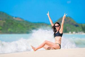 ung Lycklig kvinna i baddräkt på vit strand. skön modell i bikini Sammanträde ner. foto