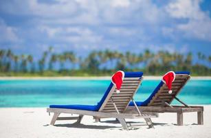 två solstolar med röd santa hattar på tropisk strand med vit sand och turkos vatten foto