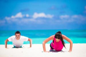 ung kondition par håller på med armhävningar under utomhus- korsa Träning träna på tropisk strand foto