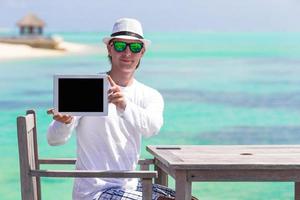 ung man på de strand med läsplatta dator. som visar skärm digital pc foto