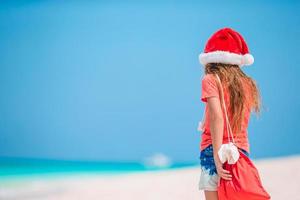 bedårande liten flicka i santa hatt på tropisk strand foto