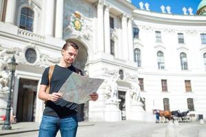 man turist med en stad Karta och ryggsäck i Europa gata. caucasian pojke ser med Karta av europeisk stad. foto