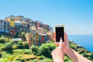 närbild av smartphone bakgrund av gammal italiensk by i cinque terre. man använder sig av mobil smartphone. foto