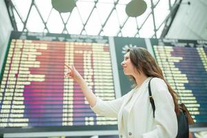 ung kvinna i internationell flygplats ser på de flyg information styrelse kontroll för flyg foto