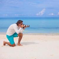 profil av ung man med kamera i hand på skön vit sandig strand foto