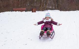 förtjusande liten Lycklig flicka ha roligt i vinter- snöig dag foto