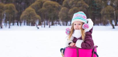 förtjusande liten Lycklig flicka sledding i vinter- snöig dag foto