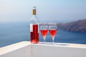 två glasögon och flaska av gott röd vin på solnedgång i grekland foto