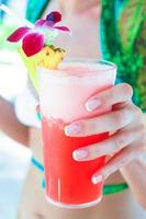 tropisk röd cocktail i hand av en ung kvinna på ett exotisk tillflykt foto