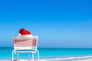 närbild röd santa hatt på stol longue på tropisk strand foto