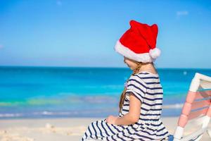 liten förtjusande flicka bär santa hatt på tropisk strand foto